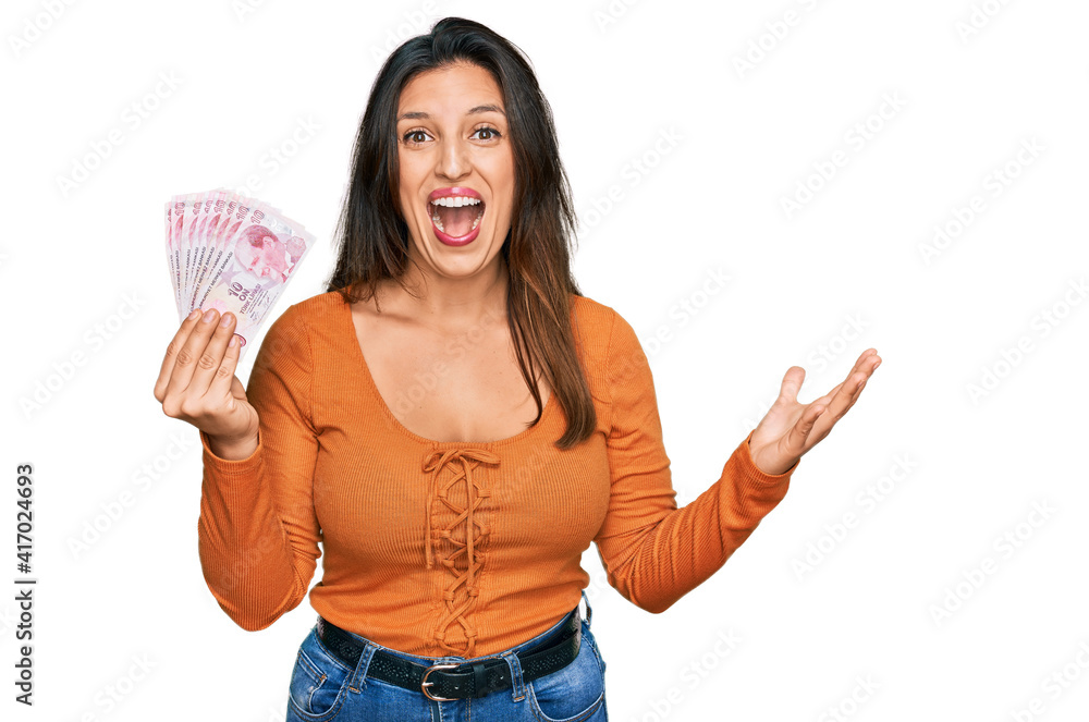 Beautiful hispanic woman holding 50 turkish lira banknotes celebrating victory with happy smile and winner expression with raised hands Beautiful hispanic woman holding 50 turkish lira banknotes celebrating victory with happy smile and winner expression with raised hands