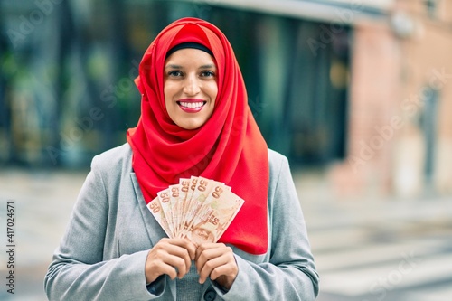 Young arab woman wearing hijab holding turkish lira banknotes at the city.
