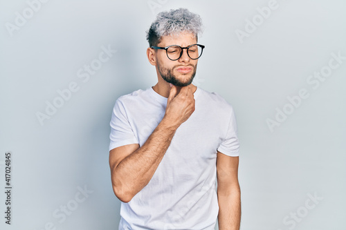Young hispanic man with modern dyed hair wearing white t shirt and glasses touching painful neck, sore throat for flu, clod and infection © Krakenimages.com
