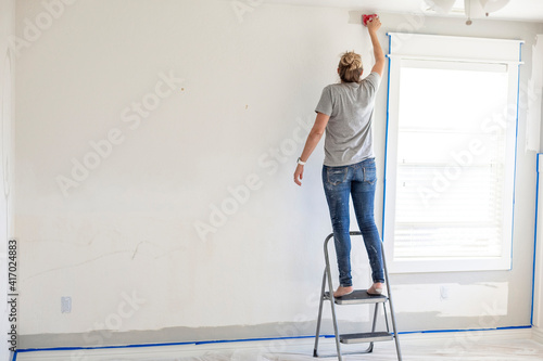 Rear view of a Woman re-painting the interior of her home. Lots of copy space on a gray and white bedroom wall