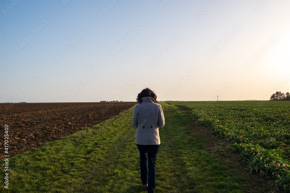 Girl with a coat between two field at dawn