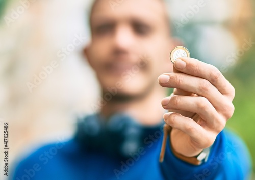 Young hispanic man using headphones holding 1 euro coin at the city © Krakenimages.com