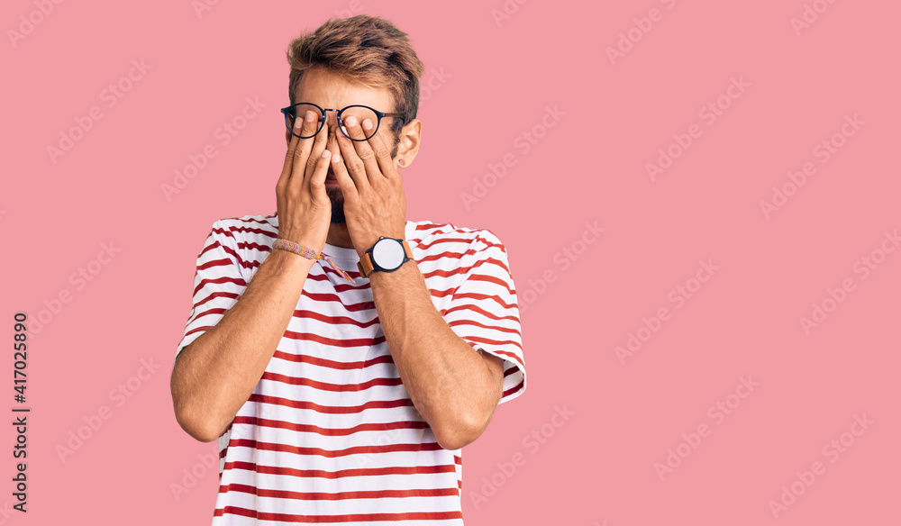 Handsome blond man with beard wearing casual clothes and glasses rubbing eyes for fatigue and headache, sleepy and tired expression. vision problem Handsome blond man with beard wearing casual clothes and glasses rubbing eyes for fatigue and headache, sleepy and tired expression. vision problem