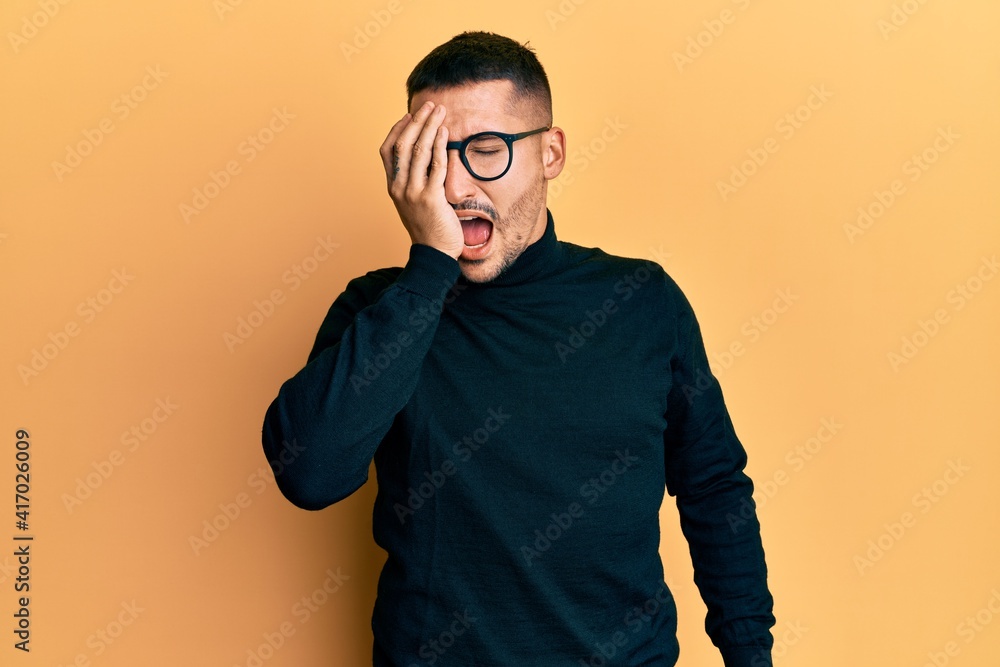 Handsome man with tattoos wearing turtleneck sweater and glasses yawning tired covering half face, eye and mouth with hand. face hurts in pain. Handsome man with tattoos wearing turtleneck sweater and glasses yawning tired covering half face, eye and mouth with hand. face hurts in pain.