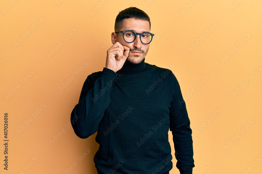Handsome man with tattoos wearing turtleneck sweater and glasses mouth and lips shut as zip with fingers. secret and silent, taboo talking Handsome man with tattoos wearing turtleneck sweater and glasses mouth and lips shut as zip with fingers. secret and silent, taboo talking