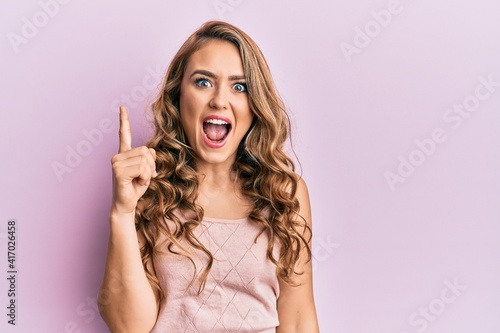 Young blonde girl wearing casual clothes pointing finger up with successful idea. exited and happy. number one.