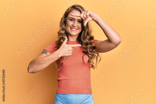 Young blonde girl wearing casual clothes smiling making frame with hands and fingers with happy face. creativity and photography concept.