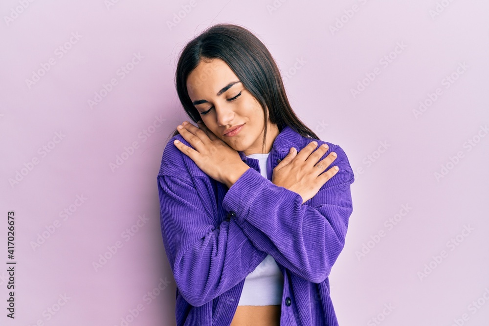 Fototapeta premium Young brunette woman wearing casual clothes hugging oneself happy and positive, smiling confident. self love and self care