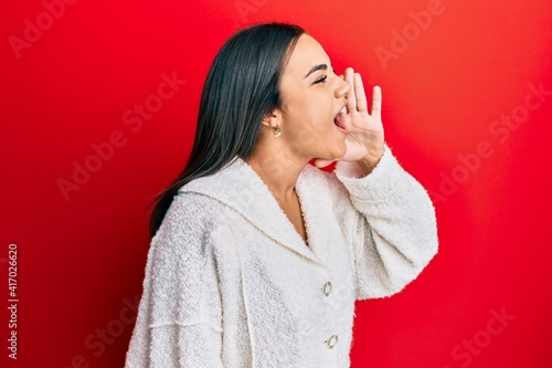 Young brunette woman wearing casual clothes shouting and screaming loud to side with hand on mouth. communication concept.