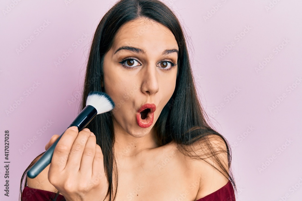 Young hispanic woman holding makeup brush and blush scared and amazed with open mouth for surprise, disbelief face Young hispanic woman holding makeup brush and blush scared and amazed with open mouth for surprise, disbelief face
