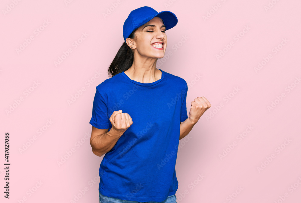 Young hispanic girl wearing delivery courier uniform excited for success with arms raised and eyes closed celebrating victory smiling. winner concept. Young hispanic girl wearing delivery courier uniform excited for success with arms raised and eyes closed celebrating victory smiling. winner concept.