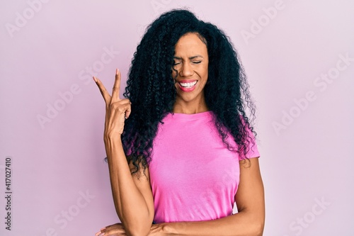 Middle age african american woman wearing casual clothes smiling with happy face winking at the camera doing victory sign. number two.
