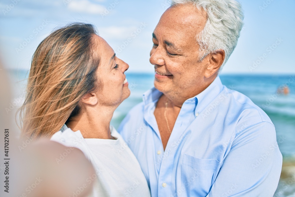 Middle age hispanic couple smiling happy making selfie by the camera at the beach. Middle age hispanic couple smiling happy making selfie by the camera at the beach.