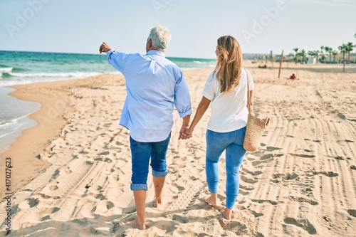 Middle age hispanic couple walking at the beach on back view.