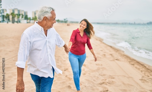 Middle age hispanic couple smiling happy walking at the beach.