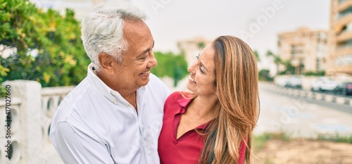 Middle age hispanic couple smiling happy and hugging walking at street.