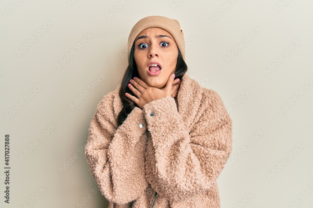 Young hispanic woman wearing wool sweater and winter hat shouting and suffocate because painful strangle. health problem. asphyxiate and suicide concept. Young hispanic woman wearing wool sweater and winter hat shouting and suffocate because painful strangle. health problem. asphyxiate and suicide concept.