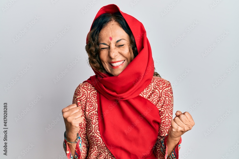 Middle age hispanic woman wearing tradition sherwani saree clothes excited for success with arms raised and eyes closed celebrating victory smiling. winner concept. Middle age hispanic woman wearing tradition sherwani saree clothes excited for success with arms raised and eyes closed celebrating victory smiling. winner concept.