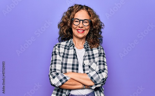 Middle age beautiful woman wearing casual shirt and glasses over isolated purple background happy face smiling with crossed arms looking at the camera. Positive person.