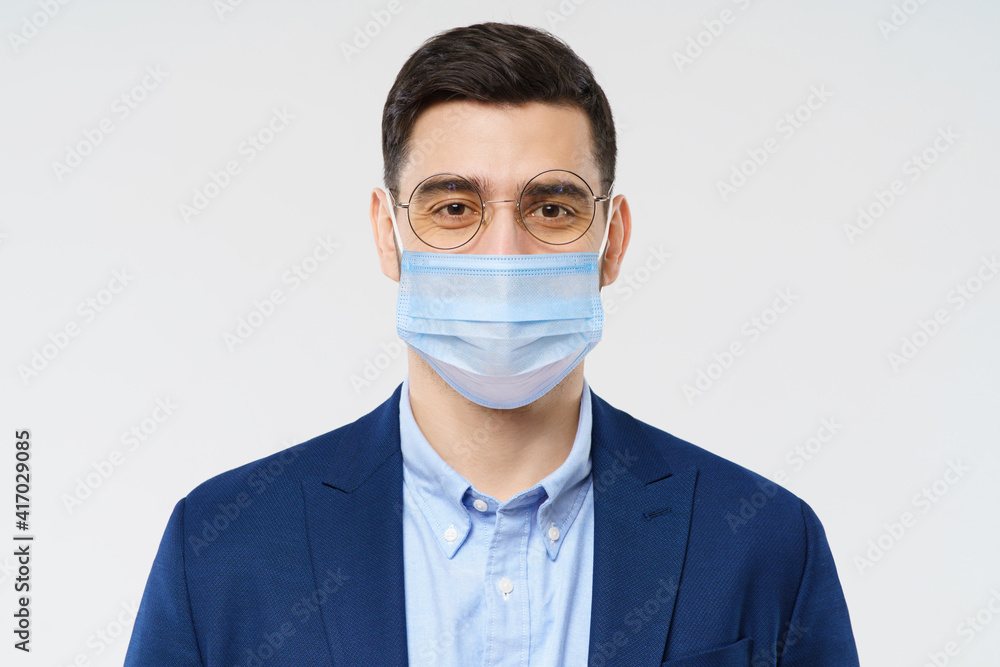 Young business man wearing medical mask, standing isolated on gray background Young business man wearing medical mask, standing isolated on gray background