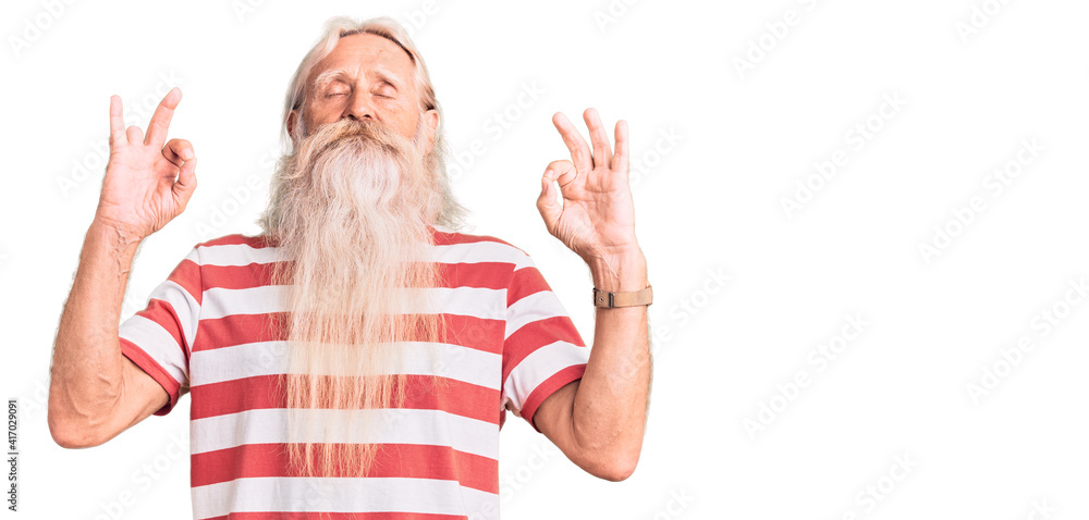 Old senior man with grey hair and long beard wearing striped tshirt relaxed and smiling with eyes closed doing meditation gesture with fingers. yoga concept. Old senior man with grey hair and long beard wearing striped tshirt relaxed and smiling with eyes closed doing meditation gesture with fingers. yoga concept.