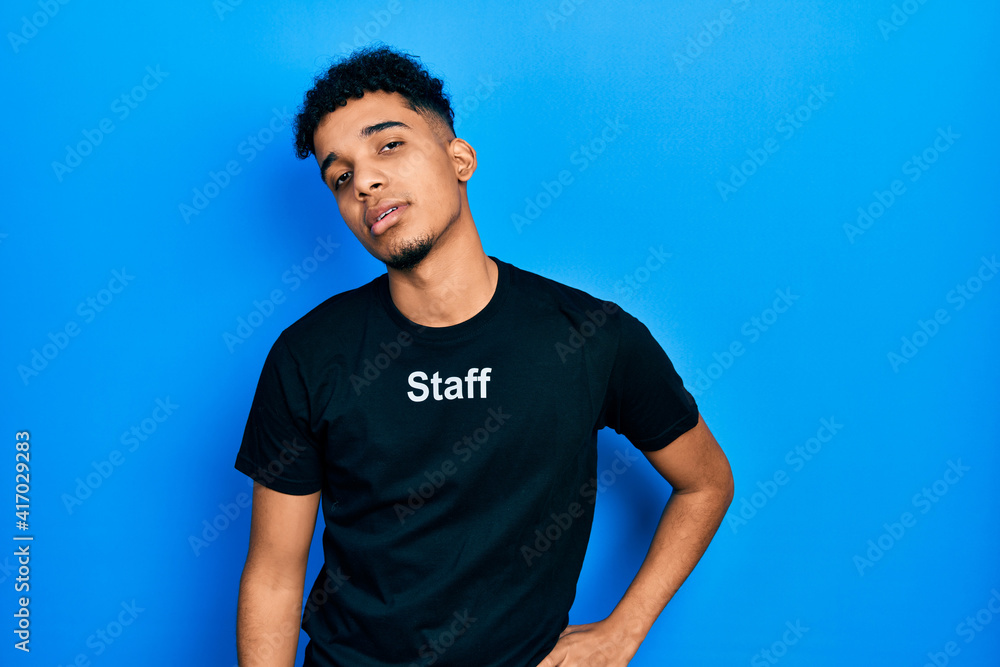 Young african american man wearing staff t shirt looking sleepy and tired, exhausted for fatigue and hangover, lazy eyes in the morning.