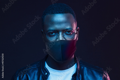 Portrait of serious african man wearing glasses leather jacket and medical mask at night