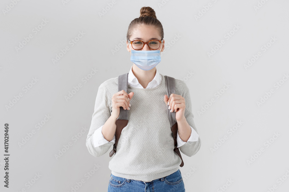 Female student wearing glasses, backpack and medical mask isolated on gray background Female student wearing glasses, backpack and medical mask isolated on gray background
