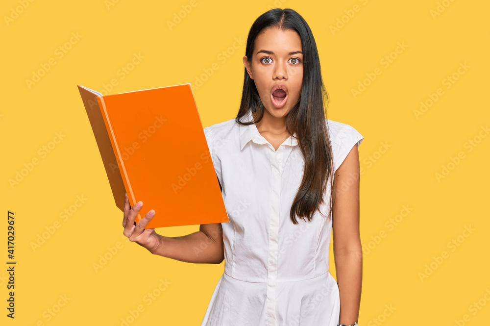 Beautiful hispanic woman reading book scared and amazed with open mouth for surprise, disbelief face Beautiful hispanic woman reading book scared and amazed with open mouth for surprise, disbelief face