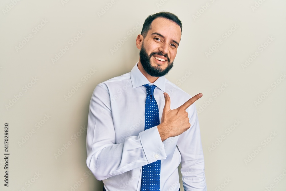 Young man with beard wearing business tie cheerful with a smile of face pointing with hand and finger up to the side with happy and natural expression on face Young man with beard wearing business tie cheerful with a smile of face pointing with hand and finger up to the side with happy and natural expression on face