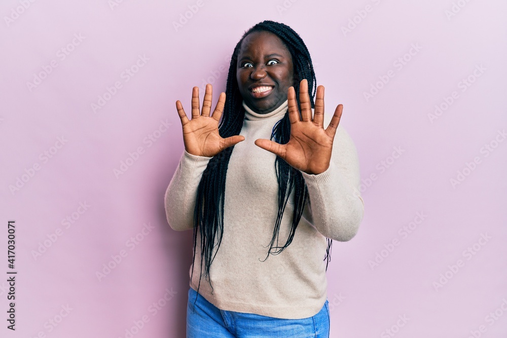 Young black woman with braids wearing casual winter sweater afraid and terrified with fear expression stop gesture with hands, shouting in shock. panic concept. Young black woman with braids wearing casual winter sweater afraid and terrified with fear expression stop gesture with hands, shouting in shock. panic concept.