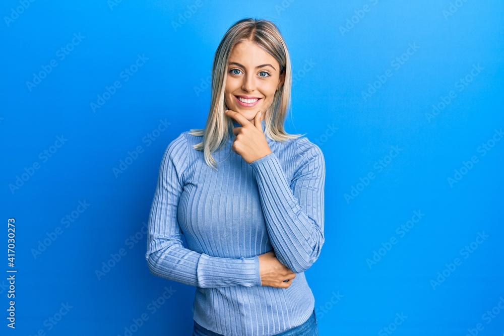 Beautiful blonde woman wearing casual clothes looking confident at the camera smiling with crossed arms and hand raised on chin. thinking positive. Beautiful blonde woman wearing casual clothes looking confident at the camera smiling with crossed arms and hand raised on chin. thinking positive.