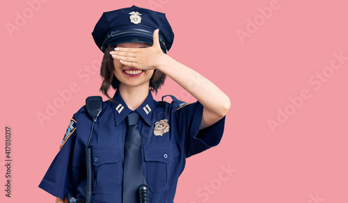 Young beautiful girl wearing police uniform smiling and laughing with hand on face covering eyes for surprise. blind concept.