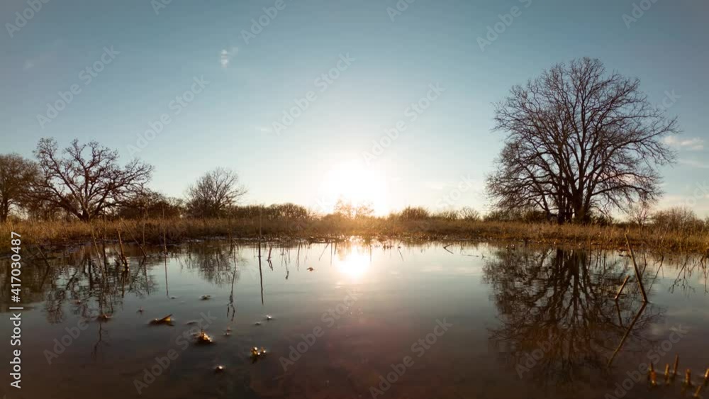 Sun setting in simple rural landscape, reflecting off a small body of water Sun setting in simple rural landscape, reflecting off a small body of water
