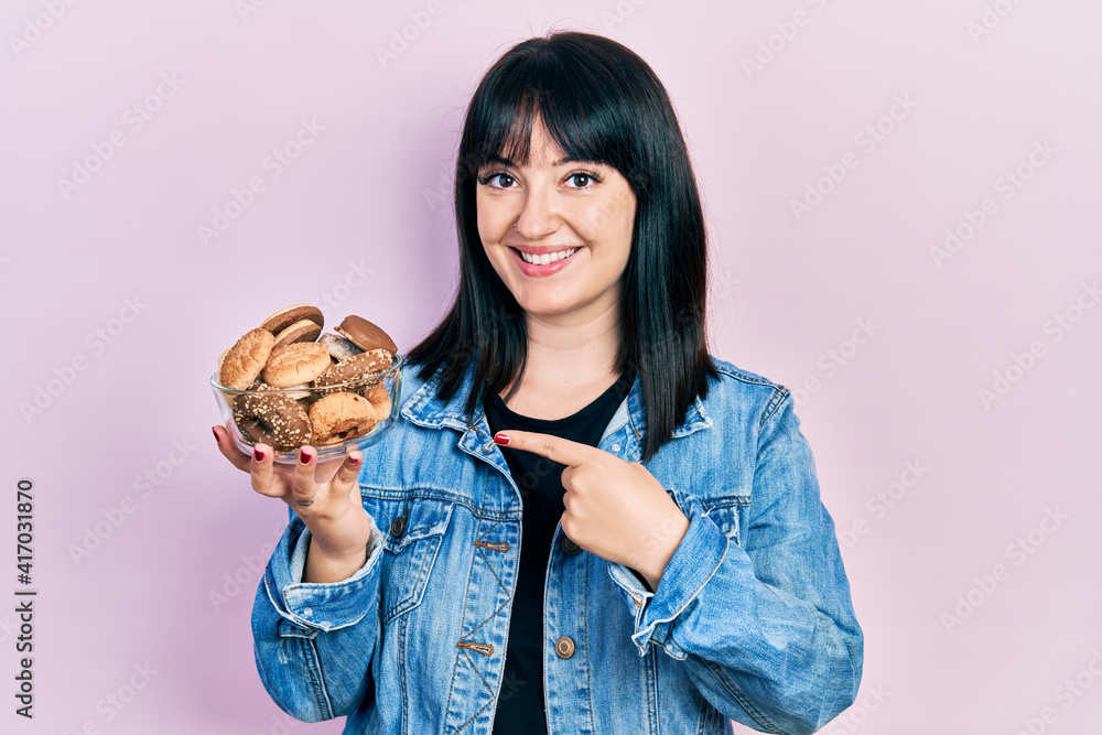 Young hispanic woman holding sweet pastries smiling happy pointing with hand and finger Young hispanic woman holding sweet pastries smiling happy pointing with hand and finger