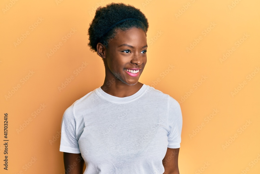 Young african american girl wearing casual white t shirt looking to side, relax profile pose with natural face and confident smile. Young african american girl wearing casual white t shirt looking to side, relax profile pose with natural face and confident smile.