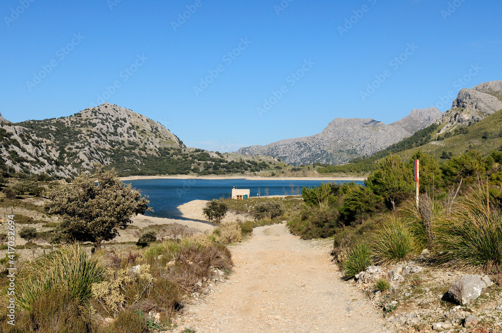 Hiking On The Trail To The Mount L'Ofre Looking Backward To The Lake Cuber In The Tramuntana Mountains On Balearic Island Mallorca On A Sunny Winter Day With A Clear Blue Sky