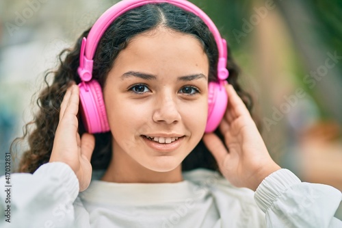Hispanic child girl smiling happy using headphones at the city.
