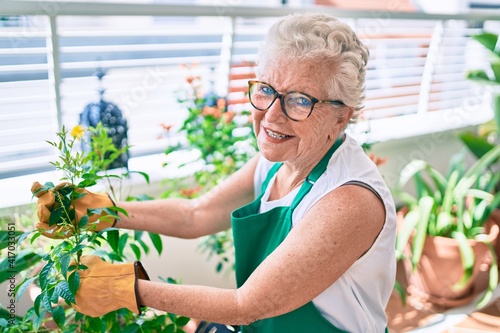 Senior woman with grey hair wearing gloves and gardener apron gardening the plants at home