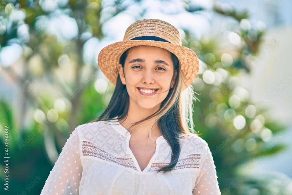 Young hispanic tourist woman wearing summer hat standing at the park.