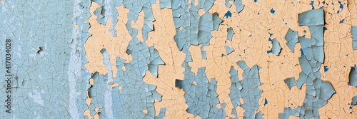 Peeling paint on the wall. Panorama of a concrete wall with old cracked flaking paint. Weathered rough painted surface with patterns of cracks and peeling. Wide panoramic grungy texture for background