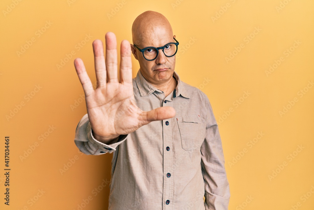 Middle age bald man wearing casual clothes and glasses doing stop sing with palm of the hand. warning expression with negative and serious gesture on the face. Middle age bald man wearing casual clothes and glasses doing stop sing with palm of the hand. warning expression with negative and serious gesture on the face.