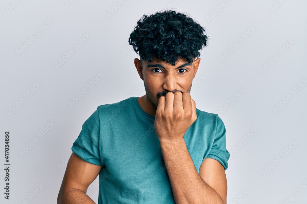 Young arab handsome man wearing casual clothes looking stressed and nervous with hands on mouth biting nails. anxiety problem. Young arab handsome man wearing casual clothes looking stressed and nervous with hands on mouth biting nails. anxiety problem.