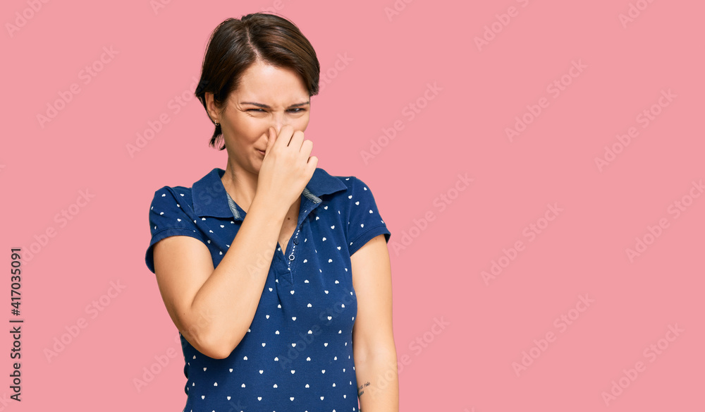 Young brunette woman with short hair wearing casual clothes smelling something stinky and disgusting, intolerable smell, holding breath with fingers on nose. bad smell Young brunette woman with short hair wearing casual clothes smelling something stinky and disgusting, intolerable smell, holding breath with fingers on nose. bad smell