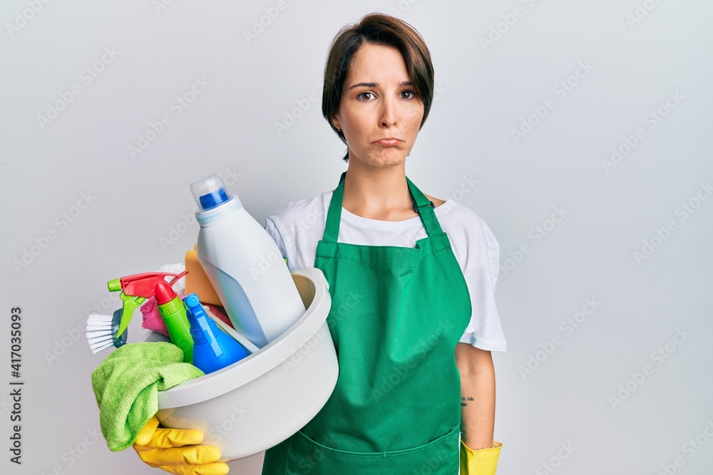 Young brunette woman with short hair wearing apron holding cleaning products depressed and worry for distress, crying angry and afraid. sad expression. Young brunette woman with short hair wearing apron holding cleaning products depressed and worry for distress, crying angry and afraid. sad expression.