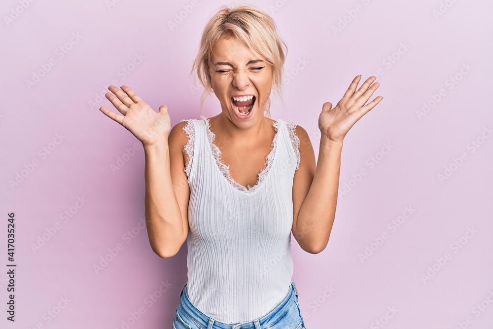 Young blonde girl wearing casual clothes celebrating mad and crazy for success with arms raised and closed eyes screaming excited. winner concept Young blonde girl wearing casual clothes celebrating mad and crazy for success with arms raised and closed eyes screaming excited. winner concept