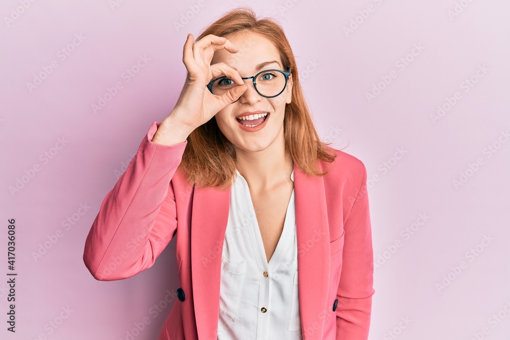 Young caucasian woman wearing business style and glasses doing ok gesture with hand smiling, eye looking through fingers with happy face.