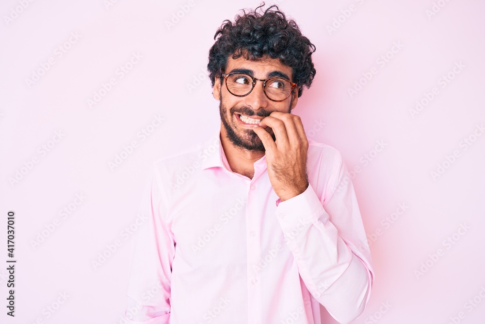 Handsome young man with curly hair and bear wearing business shirt and glasses looking stressed and nervous with hands on mouth biting nails. anxiety problem. Handsome young man with curly hair and bear wearing business shirt and glasses looking stressed and nervous with hands on mouth biting nails. anxiety problem.