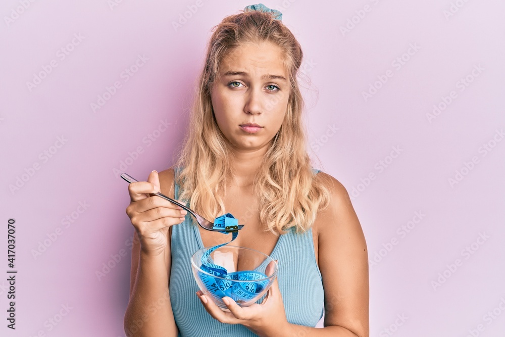 Naklejka premium Young blonde girl eating measure meter doing diet for weight loss skeptic and nervous, frowning upset because of problem. negative person.