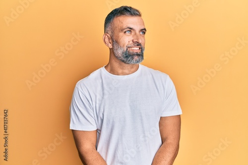 Middle age handsome man wearing casual white tshirt looking away to side with smile on face, natural expression. laughing confident.